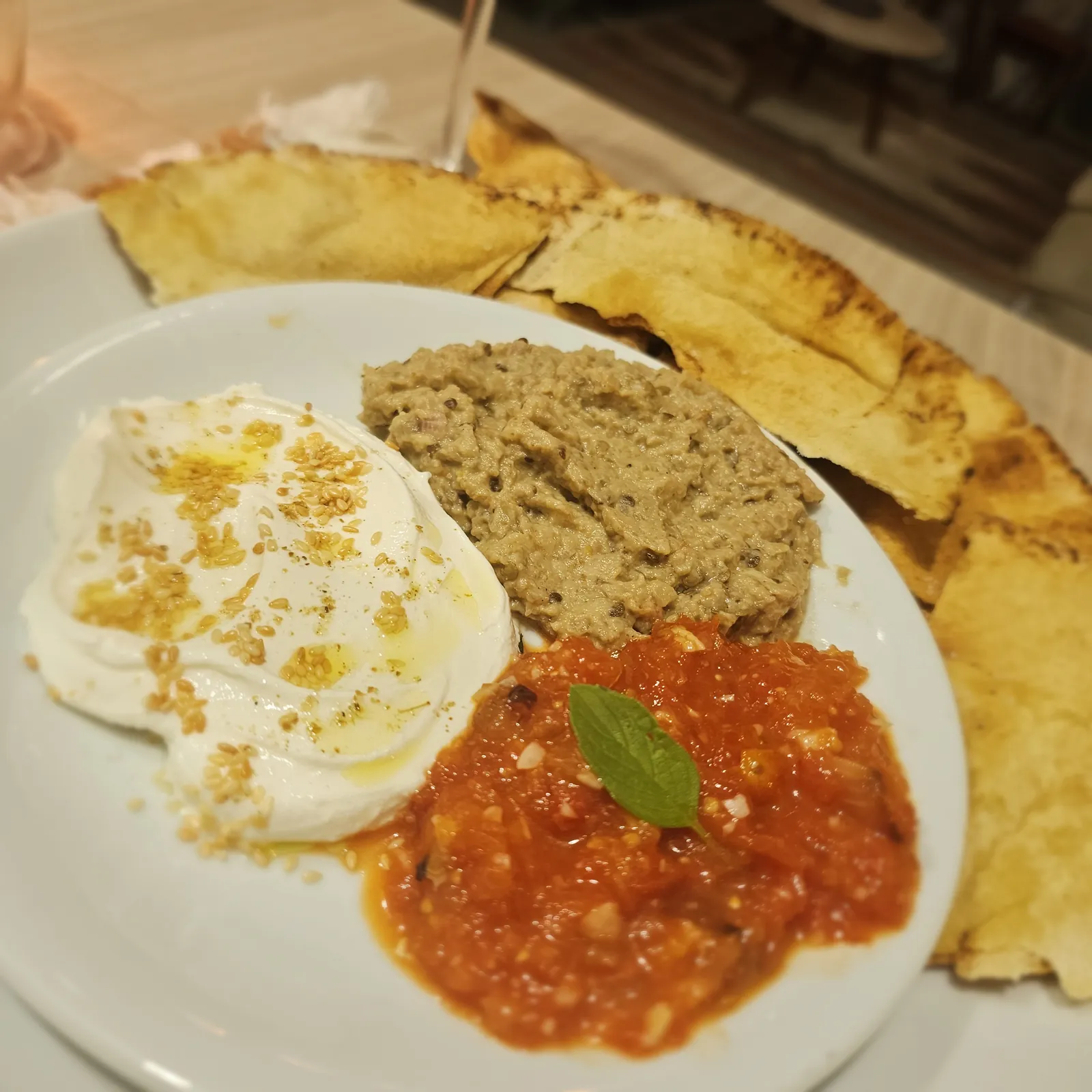 Três patês servidos em um prato com pão pita.